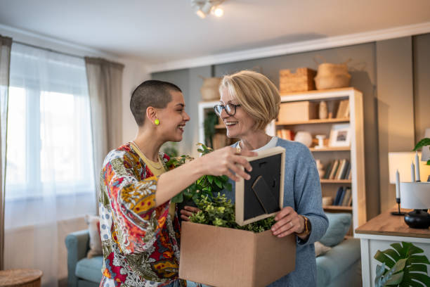 istock Two smiling women looking at photo frame while moving into new home 2199875411
