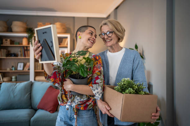 istock Two smiling women looking at photo frame while moving into new home 2199875413