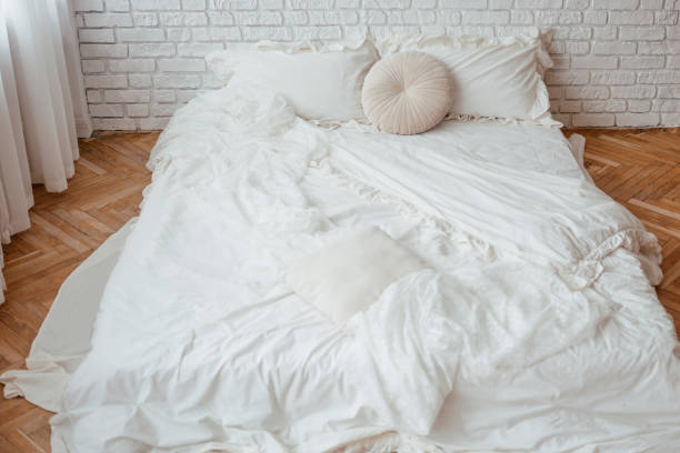 istock Cozy white bed with soft pillows and textured throw in a bright room 2199877508