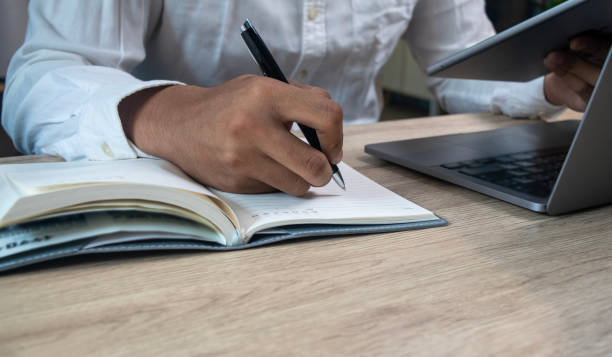 istock Men hand using pen writing on paper notebook homework on table and holding tablet search information education,Student online learning concepts 2199908191