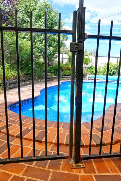 A garden lawn with stepping stones leading to a gated pool area, bordered by sheds and greenery, providing a cozy outdoor environment amidst trees and pastoral charm.