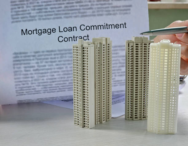 istock Miniature buildings stand on a desk beside a mortgage loan commitment contract, emphasizing the connection between financing and real estate development. concept 2199915360