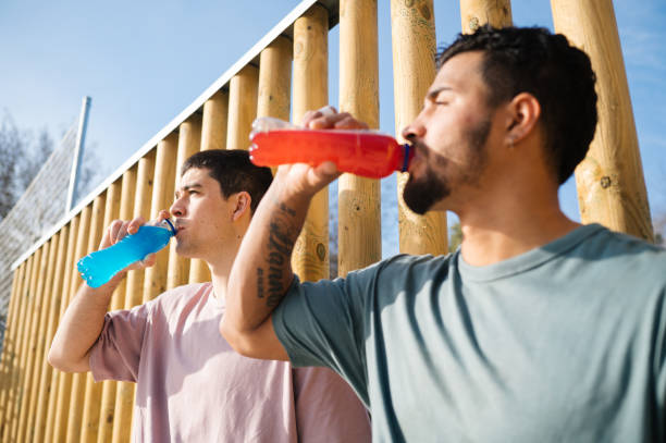 Two young basketball players drinking refreshing energy drinks after a match on a sunny day