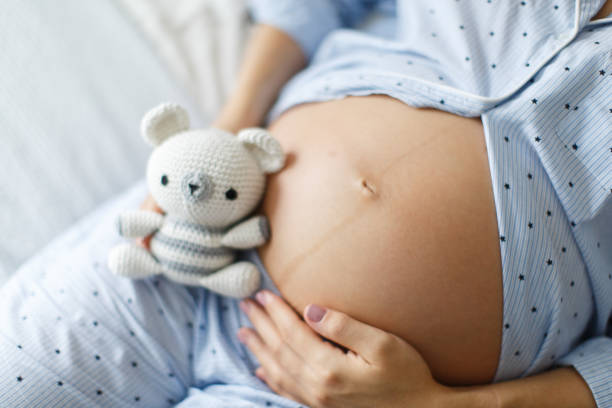 istock Expecting Mother Holding a Small Knitted Toy on Her Lap While Gently Touching Her Baby Bump 2199918185