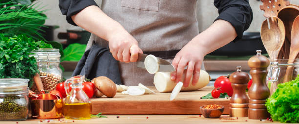 istock Food blogger chef cuts white radish. Cozy kitchen with wooden table, kitchenware, vegetables, herbs and ingredients for cooking. Healthy vegan eating, culinary, recipes, blogging 2199919242