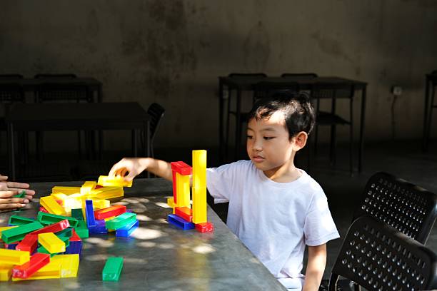 istock A young boy in a white shirt plays with colorful building blocks, stacking them on a table in a bright room.\ 2199927659
