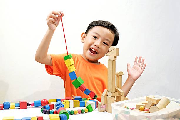 A young boy intently threads colorful wooden beads, developing fine motor skills and creativity. Perfect for educational content on child development, learning, and fun activities.
