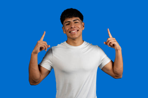 istock Young man pointing up with both index fingers on blue background 2199931774