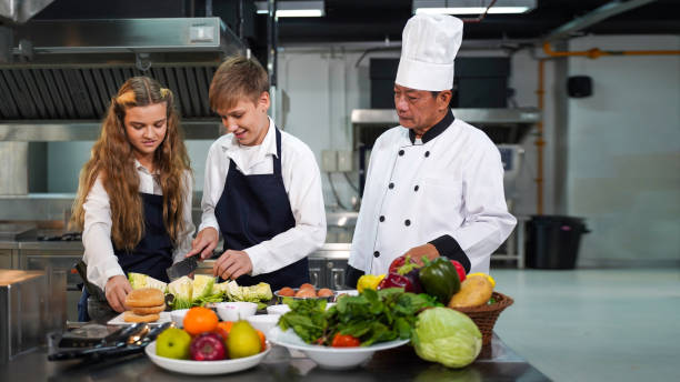 istock Chef teacher teaches cooking to the group children in class kitchen room.  Chef preparing student for learning marking 2199932571