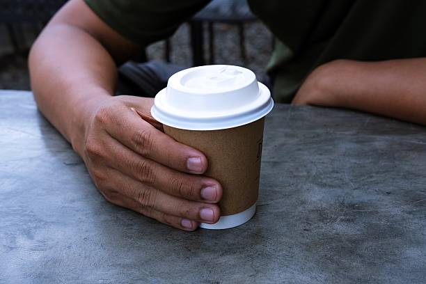 istock A person holding a takeaway coffee cup with a white lid, sitting at a table. 2199932619