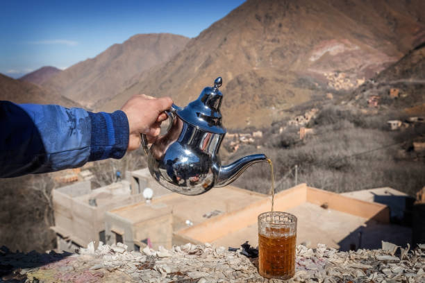 Man's hand pouring Berber tea into the cup with the mountains view Atlas mountains Morocco