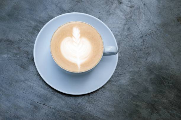 Top view of a beautifully crafted latte with intricate heart latte art in a ceramic cup and saucer on a rustic gray concrete surface,