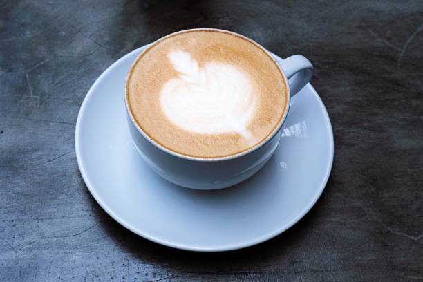 a beautifully crafted latte with intricate heart latte art in a ceramic cup and saucer on a rustic gray concrete surface,