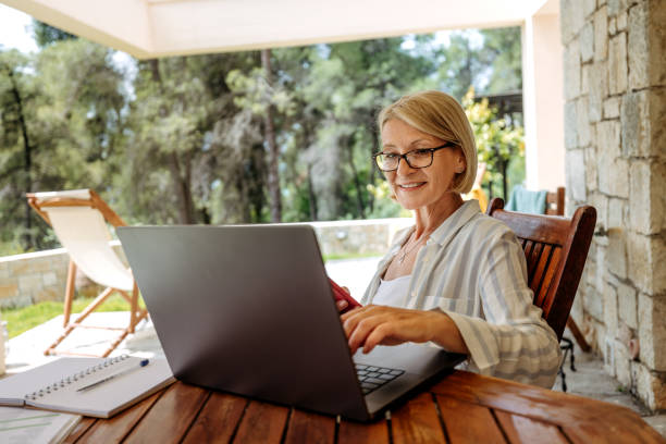 istock Smiling mature businesswoman using smart phone while working from back yard of her home 2199936122