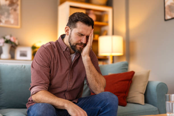 istock Closeup of man suffering from headache at home, touching his temples, copy space, blurred background. Migraine, headache, stress, tension problem, hangover concept 2199938123