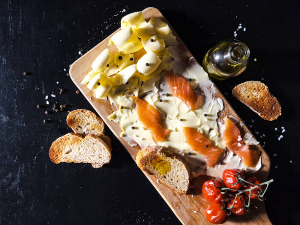 Directly above shot of butter board with salmon, tomatoes, bread and olive oil in rustic kitchen, butter board with seafood on dark table, copy space