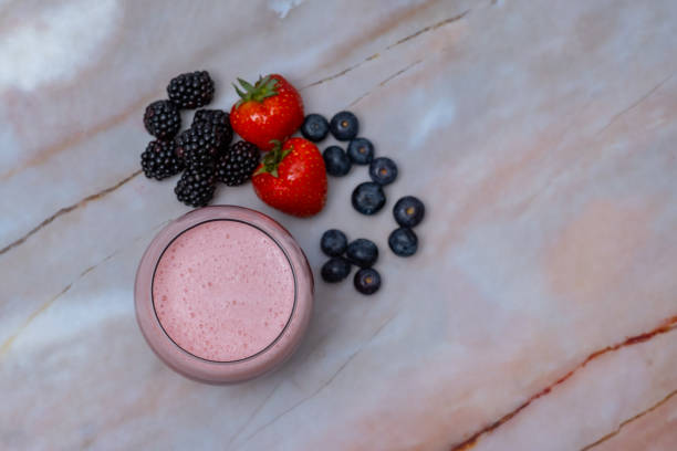 A glass of strawberry, blueberry, blackberry smoothie on a pink marble table, with some berries around it, table top view, horizontal image.