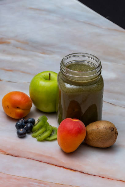 Green fruit juice made with superfood kiwi, pineapple, apple, spirulina on a pink marble table with fresh fruits around, high angle view, vertical image.
