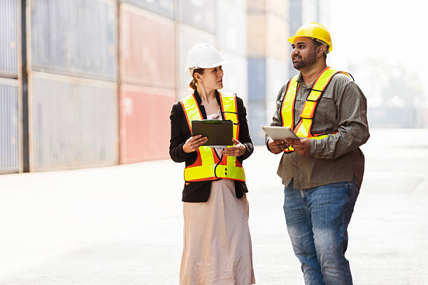 istock Two logistics professionals in safety vests and hard hats inspect shipping containers using tablets. Supply chain management, global trade, freight logistics, and industrial teamwork at a port. 2199946010