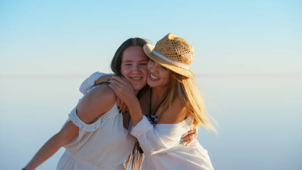happy stylish mother and teenage daughter on the beach with smartphone listening to the music with headphones and dancing.