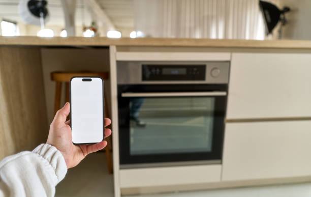 istock Hand holding smartphone with blank screen in front of oven in modern kitchen 2199953081