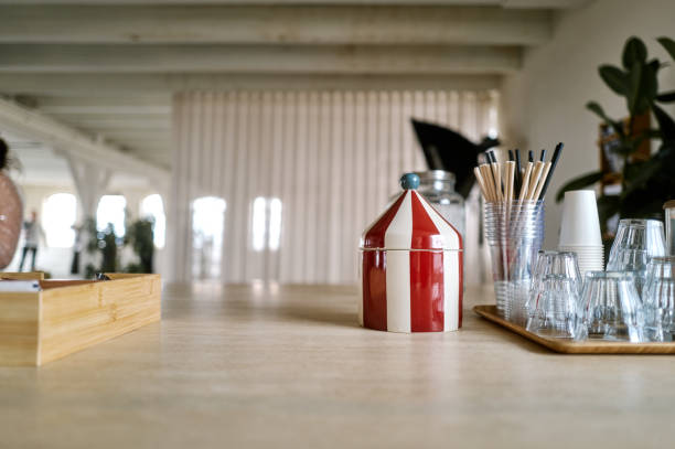 Red and white striped circus tent shaped sugar bowl sits on a table in an office break room, disposable cups, straws and glasses nearby