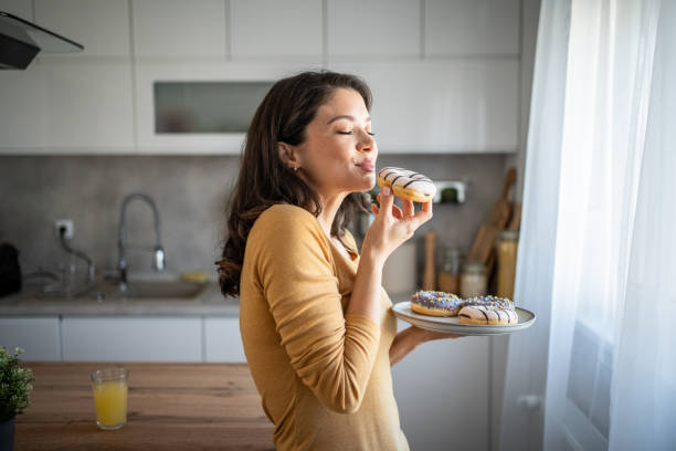 istock Happy woman relishing a donut while relaxing at home 2199961574