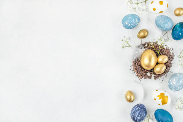 istock Easter eggs, feathers in a nest on a blue white background. Stylish golden and blue eggs. top view 2199967715