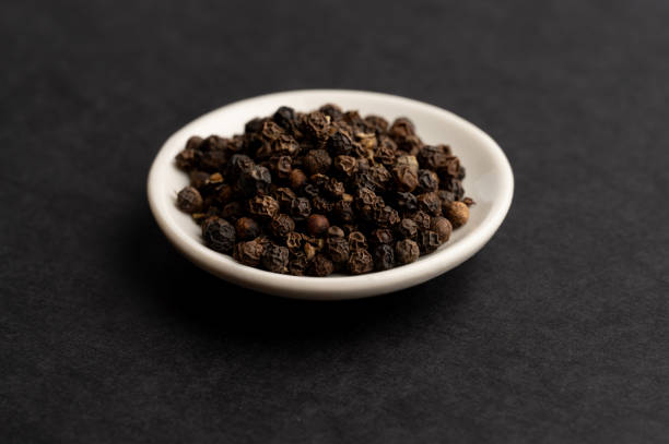 istock Black peppercorns in white bowl on dark background 2199970669