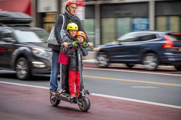 West 23rd Street, Manhattan, New York, United States - January 18th 2025:  Father and two kids with crash helmets on an electric scooter driving fast down the street