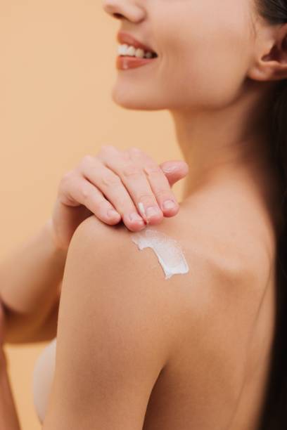 istock Smiling woman applying moisturizing cream on shoulder on a beige background. 2199990668