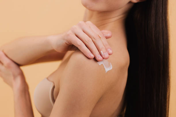istock Woman applying moisturizing cream on her shoulder on a beige background. 2199990689