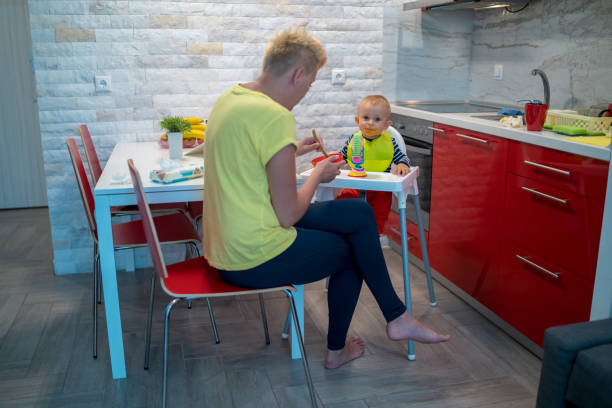 istock Mother spoon feeding her baby boy in the kitchen 2199991718