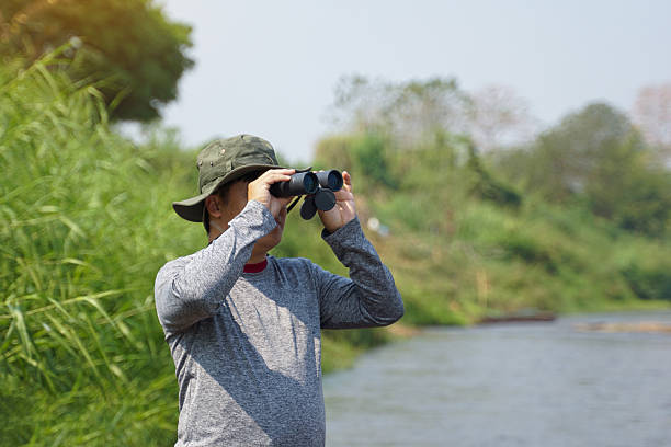 istock Asian man uses binoculars to observe local birds along a river. Soft and selective focus. 2199992635