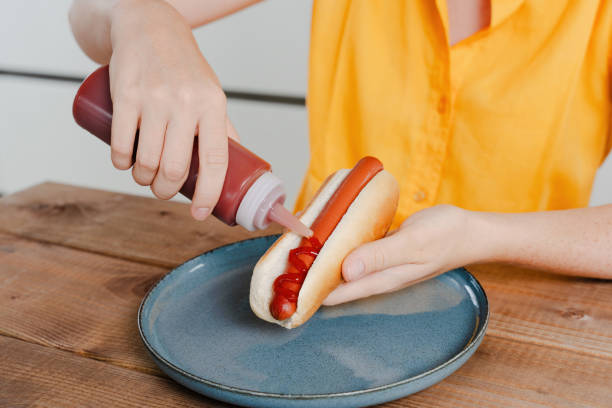 istock Person Squeezing Ketchup on Hot Dog in Bun 2199999570