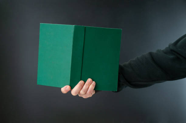 istock Man`s hand holding book with green hardcover on black background 2200002673