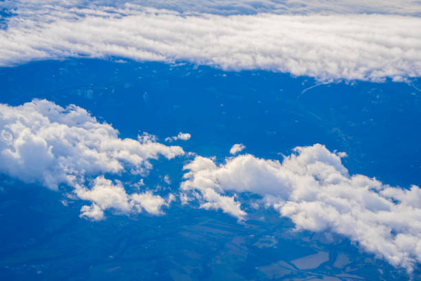Fluffy clouds drift across a vibrant blue sky, revealing patches of green fields and rugged terrain below on a clear day.