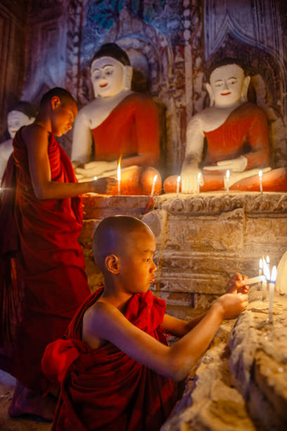 Two young buddhist monks lighting candles in a temple in bagan, myanmar