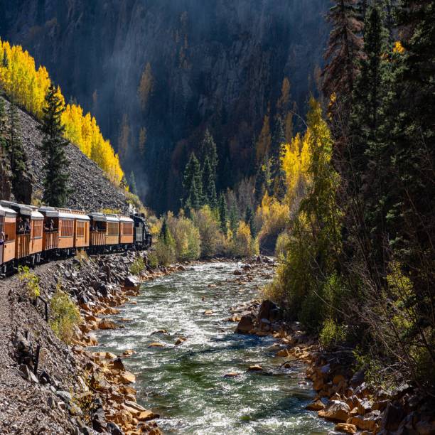 istock Train Passing Through Mountains with Fall Colors Next to a River 2200008803