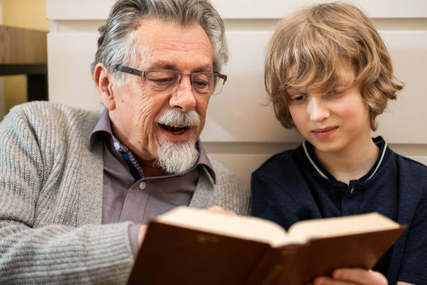istock Grandfather Reading Book with Grandson at Home 2200010554