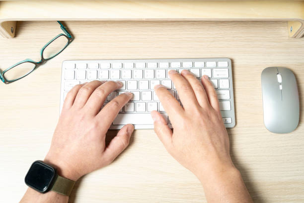 istock Office worker typing on keyboard at desk with mouse and eyeglasses 2200011158