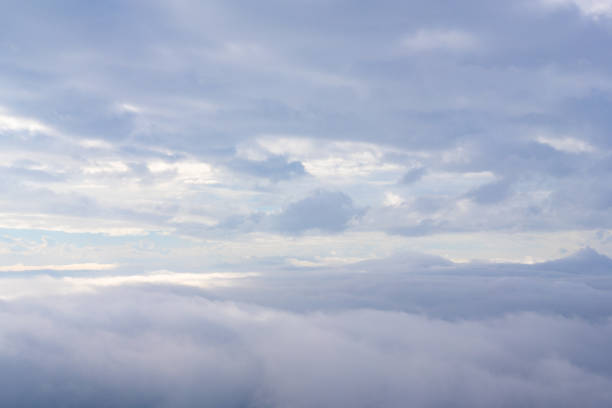 Soft clouds gently blanket a tranquil landscape, illuminated by the soft glow of the rising sun, creating a peaceful early morning vista.