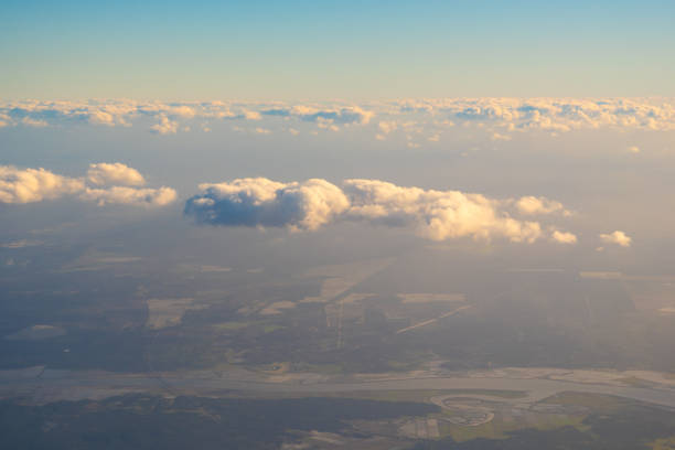 Soft clouds drift above a tranquil landscape, revealing patches of green and shimmering water under the warm glow of the setting sun.