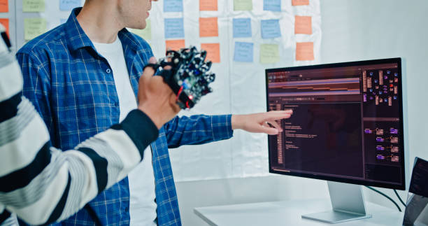 Closeup Two male engineer software developers inspecting a robotic hand prototype working on development and coding tasks with integration in office. Artificial intelligence and programming. Closeup Two male engineer software developers inspecting a robotic hand prototype working on development and coding tasks with integration in office. Artificial intelligence and programming concept. medical device engineering stock pictures, royalty-free photos & images