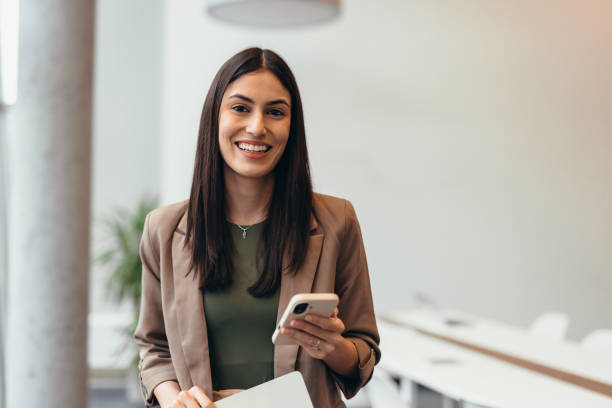 istock Young businesswoman smiling and using smartphone in modern office 2200021843