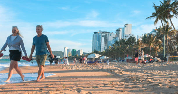 Mature couple walk along beach at sunset, islands and city in distance