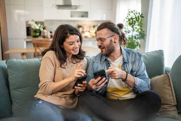 istock Cheerful young couple relaxing on sofa, browsing internet on smartphones 2200028983