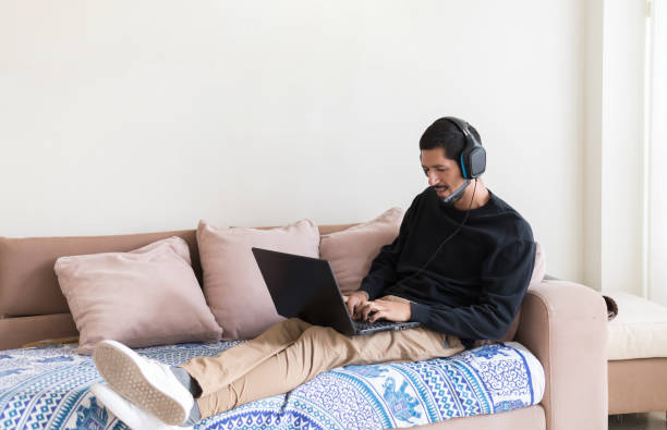istock Young man working from home on his sofa with laptop and headset 2200029090