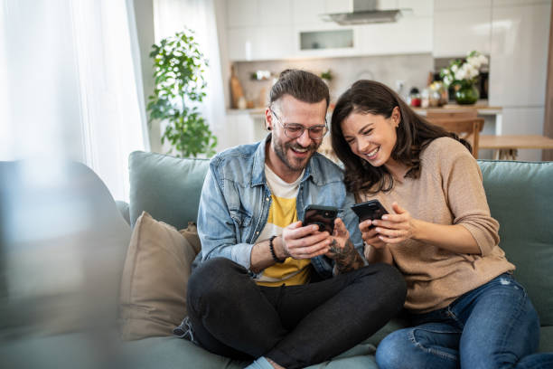 istock Cheerful young couple relaxing on sofa, browsing internet on smartphones 2200029117