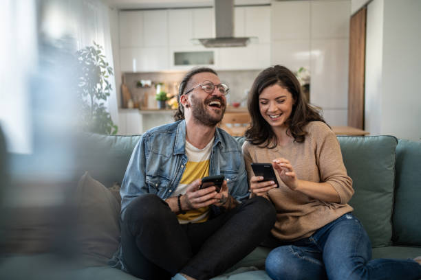 istock Cheerful young couple relaxing on sofa, browsing internet on smartphones 2200029141